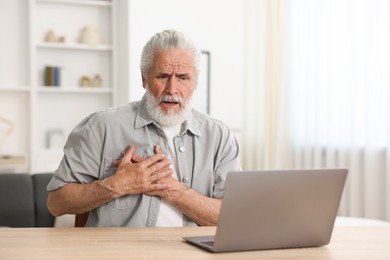 Photo of Senior man having online consultation with doctor via laptop at table indoors