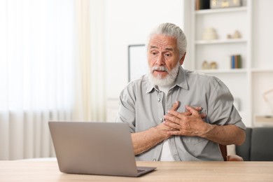 Photo of Senior man having online consultation with doctor via laptop at table indoors