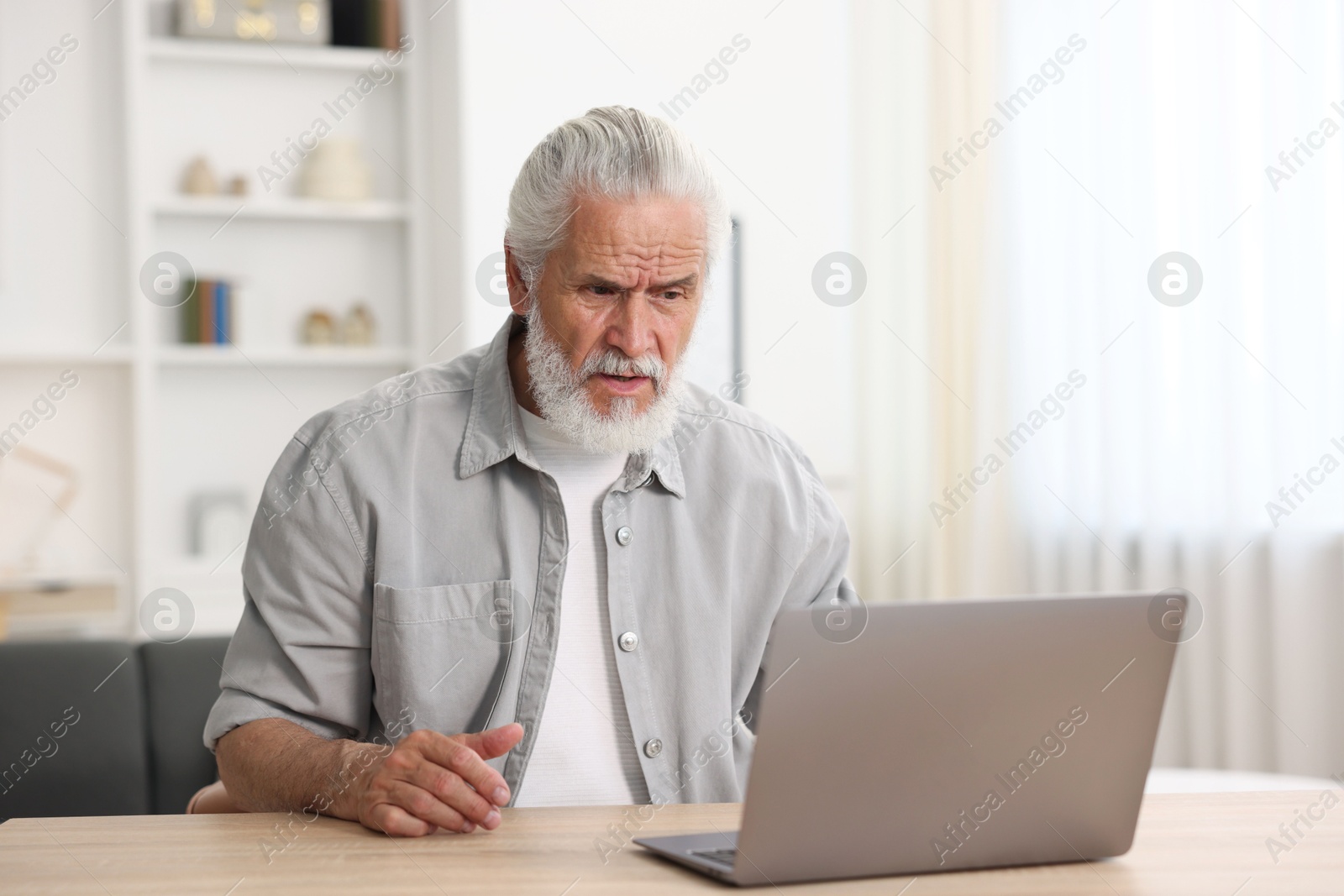 Senior man having online consultation with doctor via laptop at table indoors Photo of Senior man having online consultation with doctor via laptop at table indoors