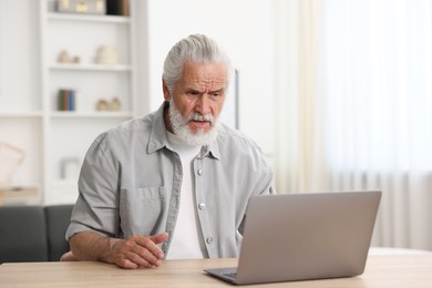 Photo of Senior man having online consultation with doctor via laptop at table indoors