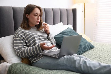 Photo of Sick woman having online consultation with doctor via laptop on bed indoors