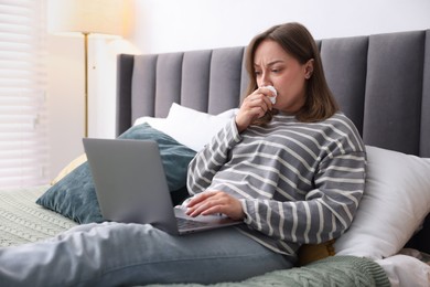 Photo of Sick woman having online consultation with doctor via laptop on bed indoors