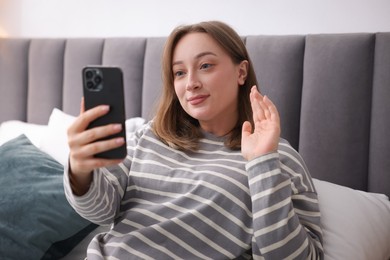 Photo of Woman having online consultation with doctor via smartphone on bed indoors