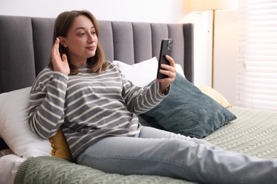 Photo of Woman having online consultation with doctor via smartphone on bed indoors