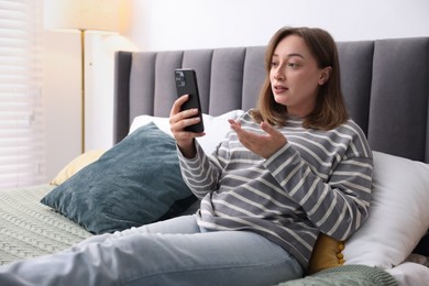 Photo of Woman having online consultation with doctor via smartphone on bed indoors