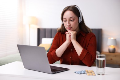Photo of Woman in headphones having online consultation with doctor via laptop at table indoors