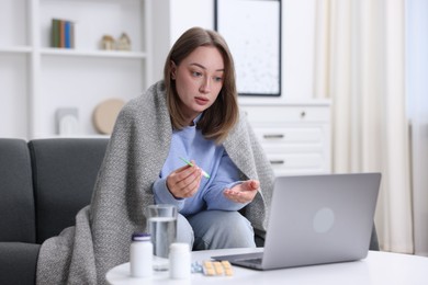 Photo of Sick woman with thermometer having online consultation with doctor via laptop at home