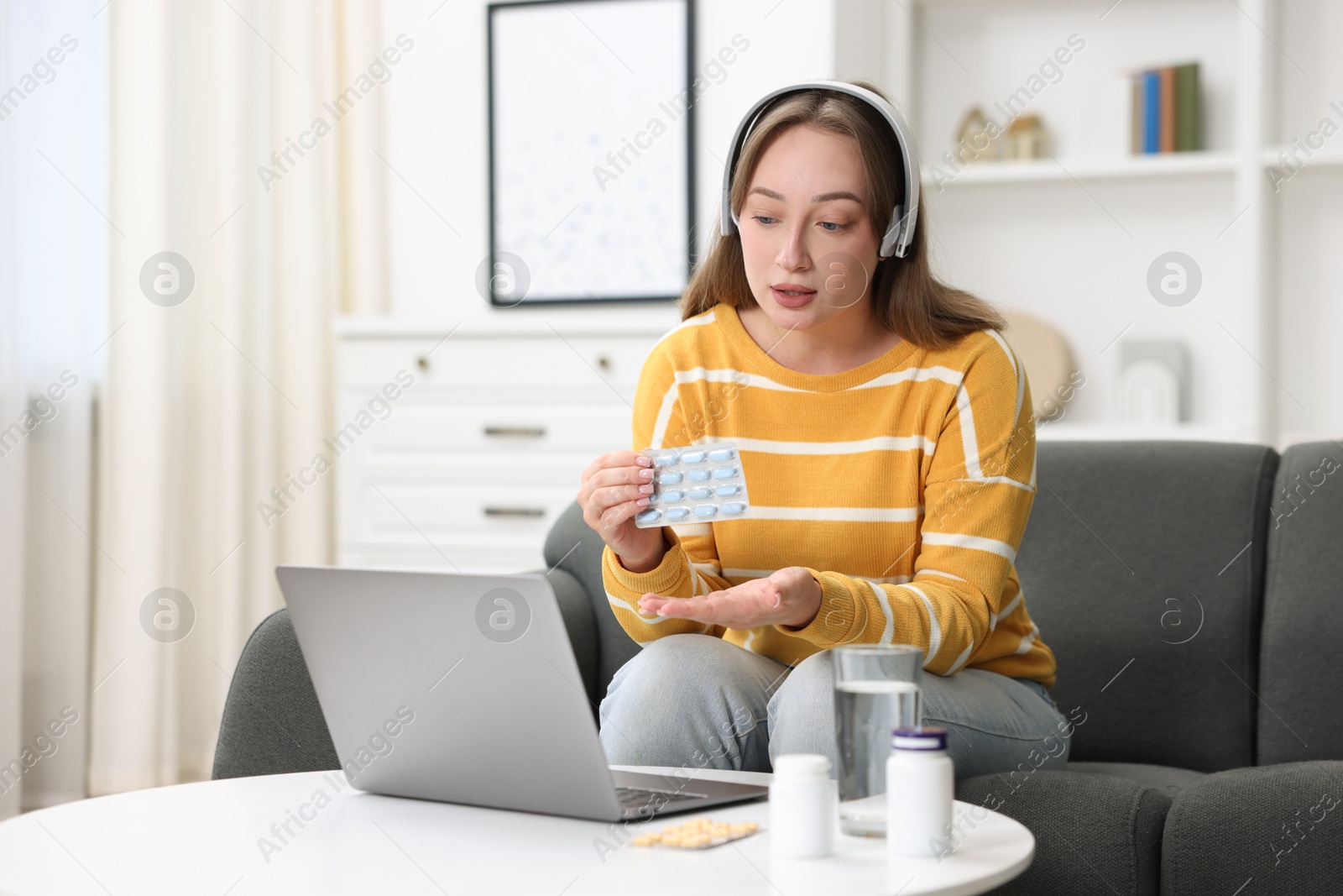 Photo of Woman in headphones with pills having online consultation with doctor via laptop at home