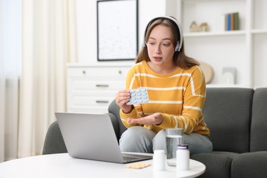 Photo of Woman in headphones with pills having online consultation with doctor via laptop at home