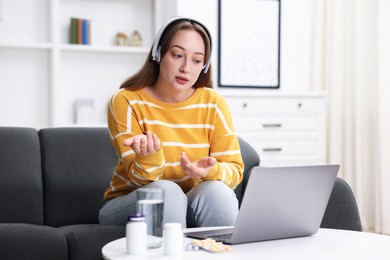 Photo of Woman in headphones having online consultation with doctor via laptop at home
