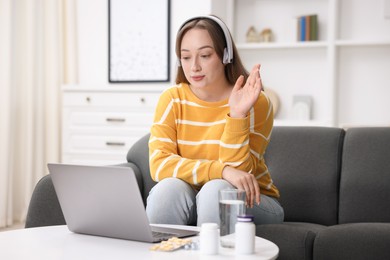 Photo of Woman in headphones having online consultation with doctor via laptop at home
