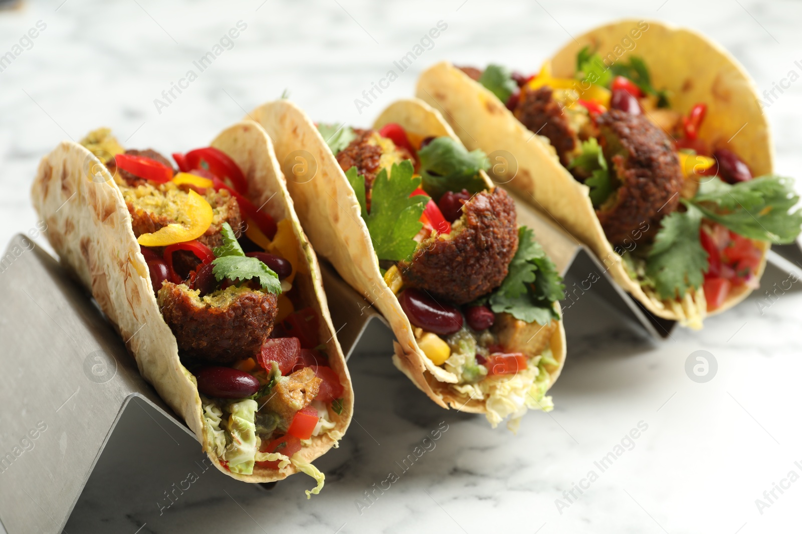 Photo of Tasty vegetarian tacos with falafel, tofu, beans and vegetables on white marble table, closeup