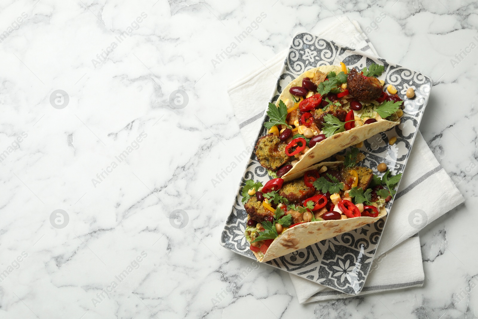 Photo of Tasty vegetarian tacos with falafel, tofu, beans and vegetables on white marble table, top view. Space for text