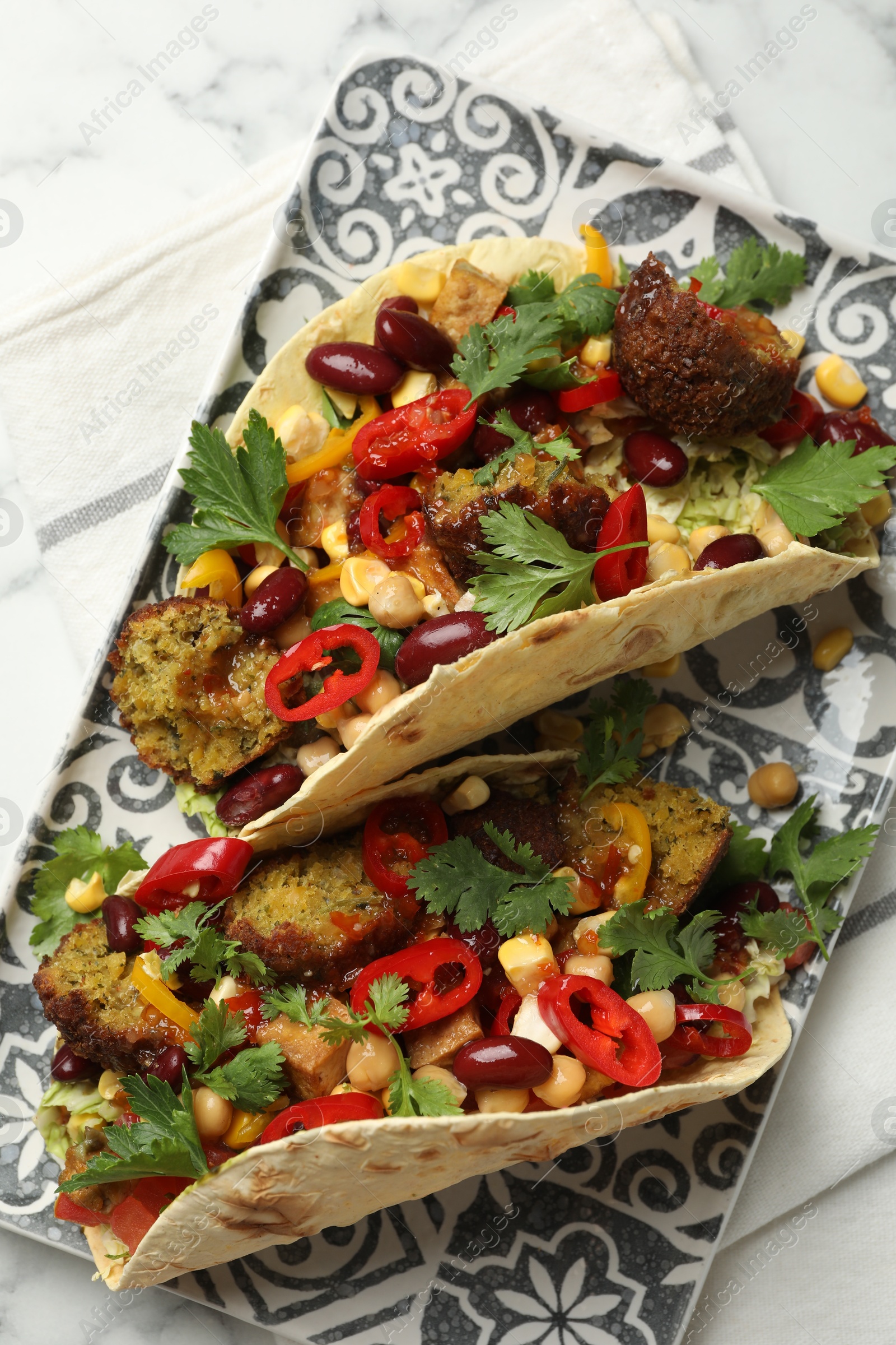 Photo of Tasty vegetarian tacos with falafel, tofu, beans and vegetables on white marble table, top view