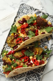 Photo of Tasty vegetarian tacos with falafel, tofu, beans and vegetables on white marble table, top view