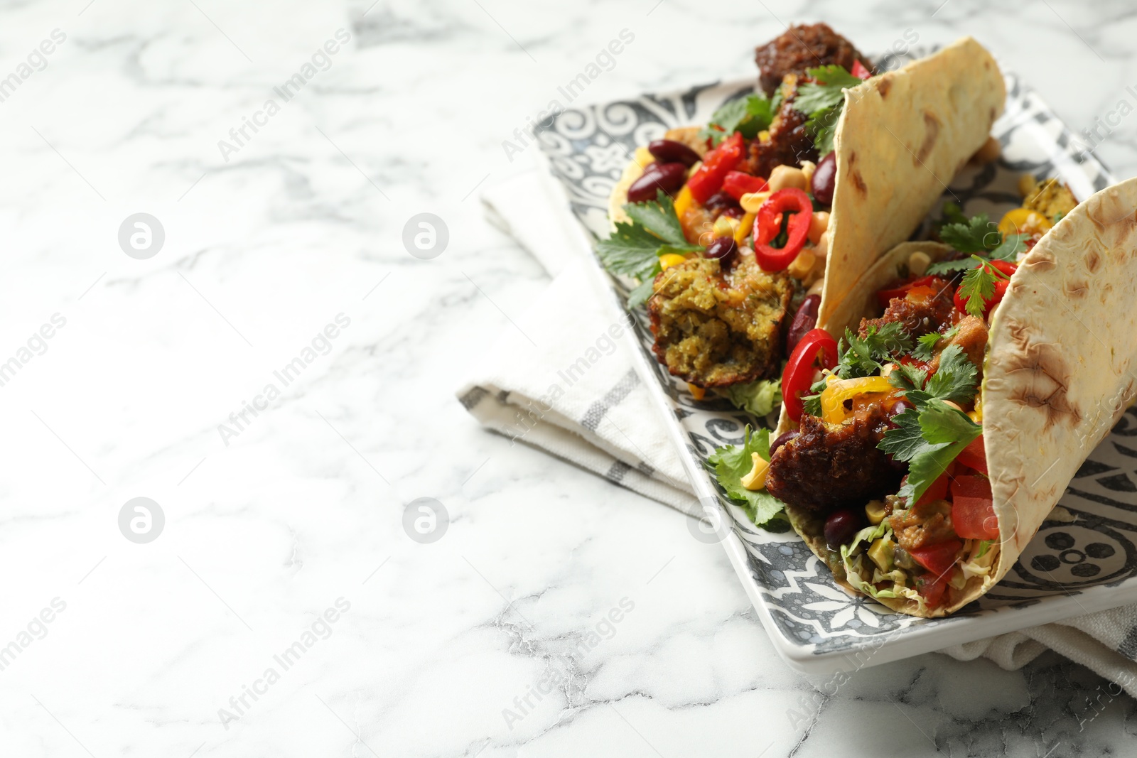 Photo of Tasty vegetarian tacos with falafel, tofu, beans and vegetables on white marble table, closeup. Space for text