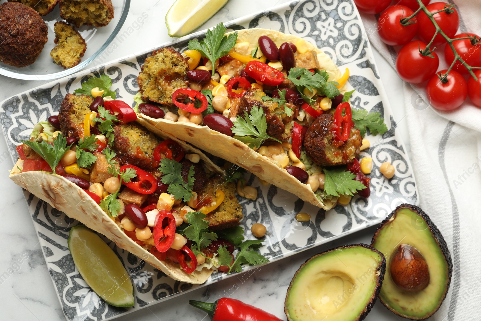 Photo of Tasty vegetarian tacos with falafel and other ingredients on white marble table, flat lay