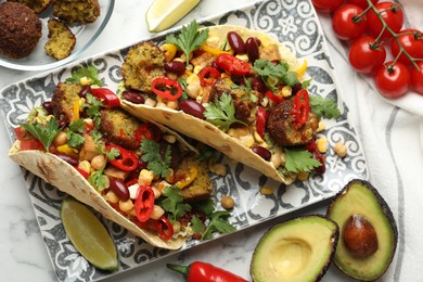 Photo of Tasty vegetarian tacos with falafel and other ingredients on white marble table, flat lay