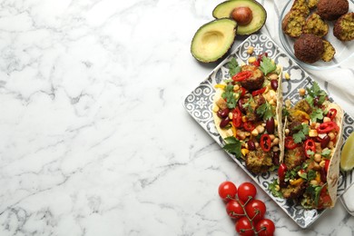 Photo of Tasty vegetarian tacos with falafel and other ingredients on white marble table, flat lay. Space for text