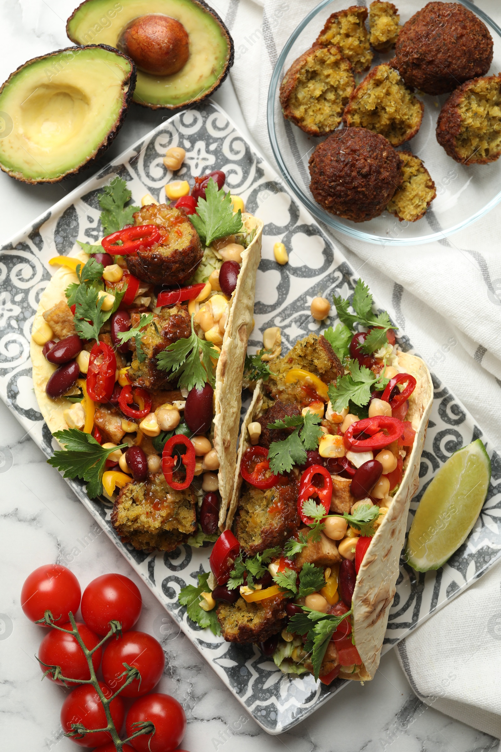 Photo of Tasty vegetarian tacos with falafel and other ingredients on white marble table, flat lay
