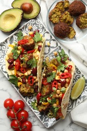 Photo of Tasty vegetarian tacos with falafel and other ingredients on white marble table, flat lay