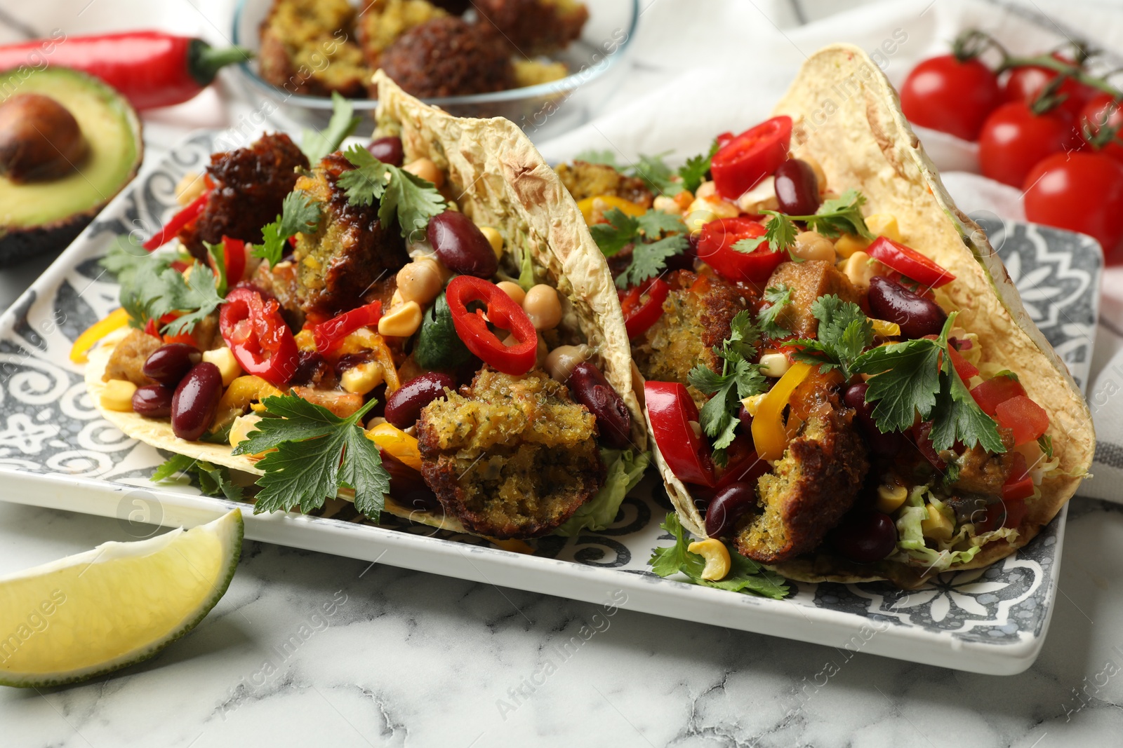 Photo of Tasty vegetarian tacos with falafel and other ingredients on white marble table, closeup