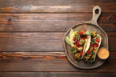Photo of Tasty vegetarian tacos with falafel served with sauce on wooden table, top view. Space for text