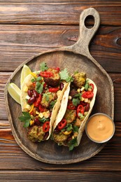 Photo of Tasty vegetarian tacos with falafel served with sauce on wooden table, top view