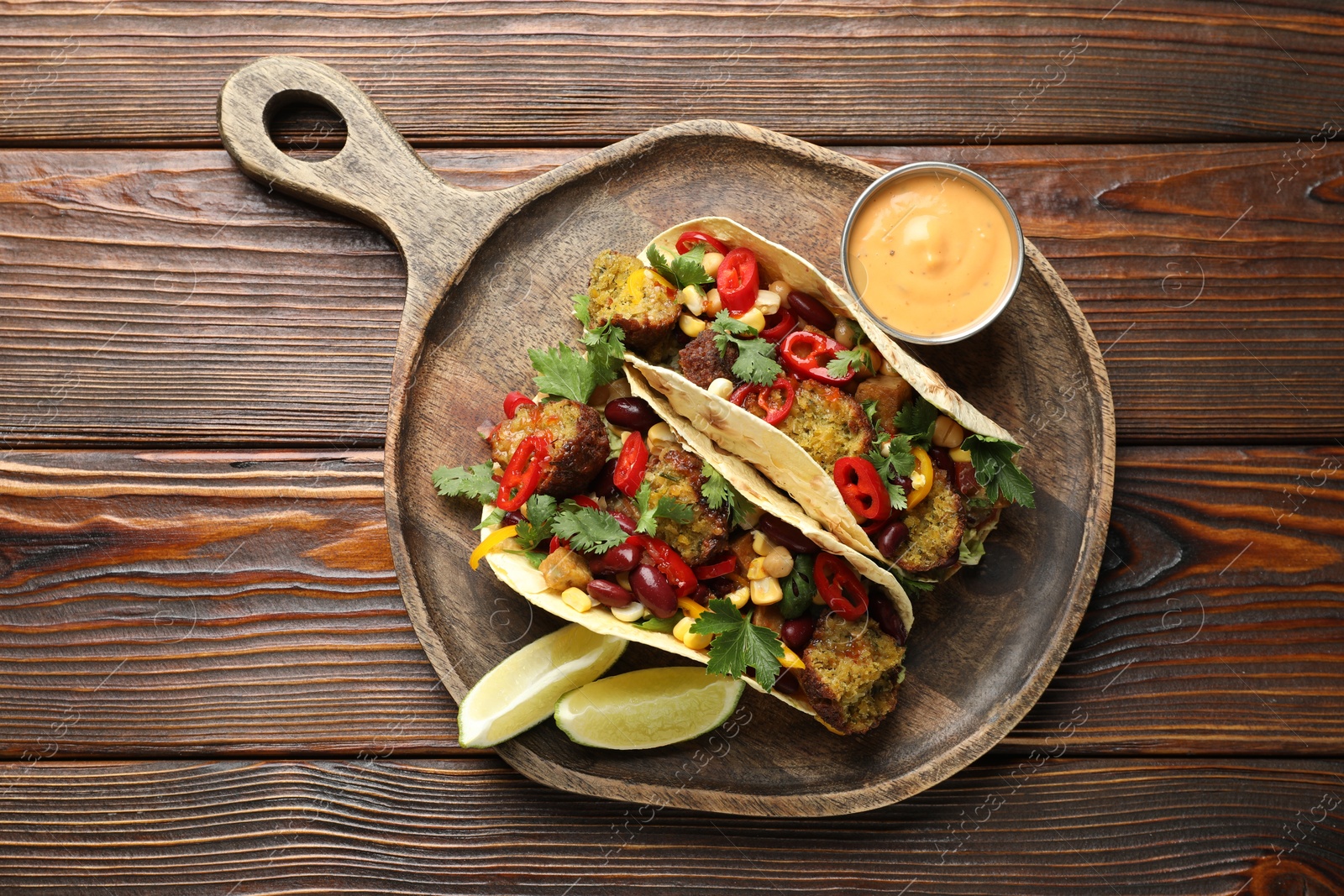 Photo of Tasty vegetarian tacos with falafel served with sauce on wooden table, top view
