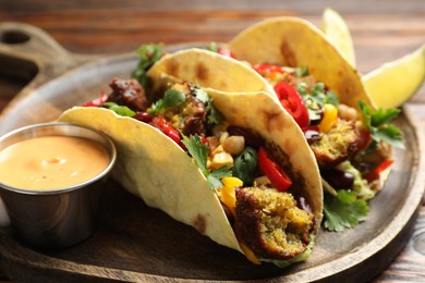 Photo of Tasty vegetarian tacos with falafel served with sauce on table, closeup