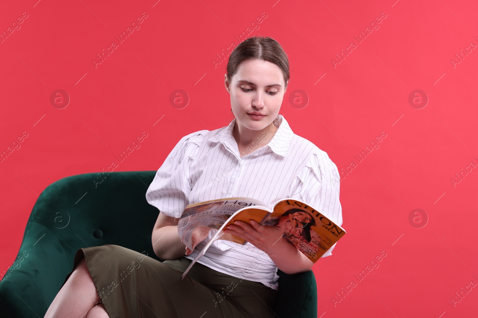 Woman with lifestyle magazine on armchair against red background Photo of Woman with lifestyle magazine on armchair against red background