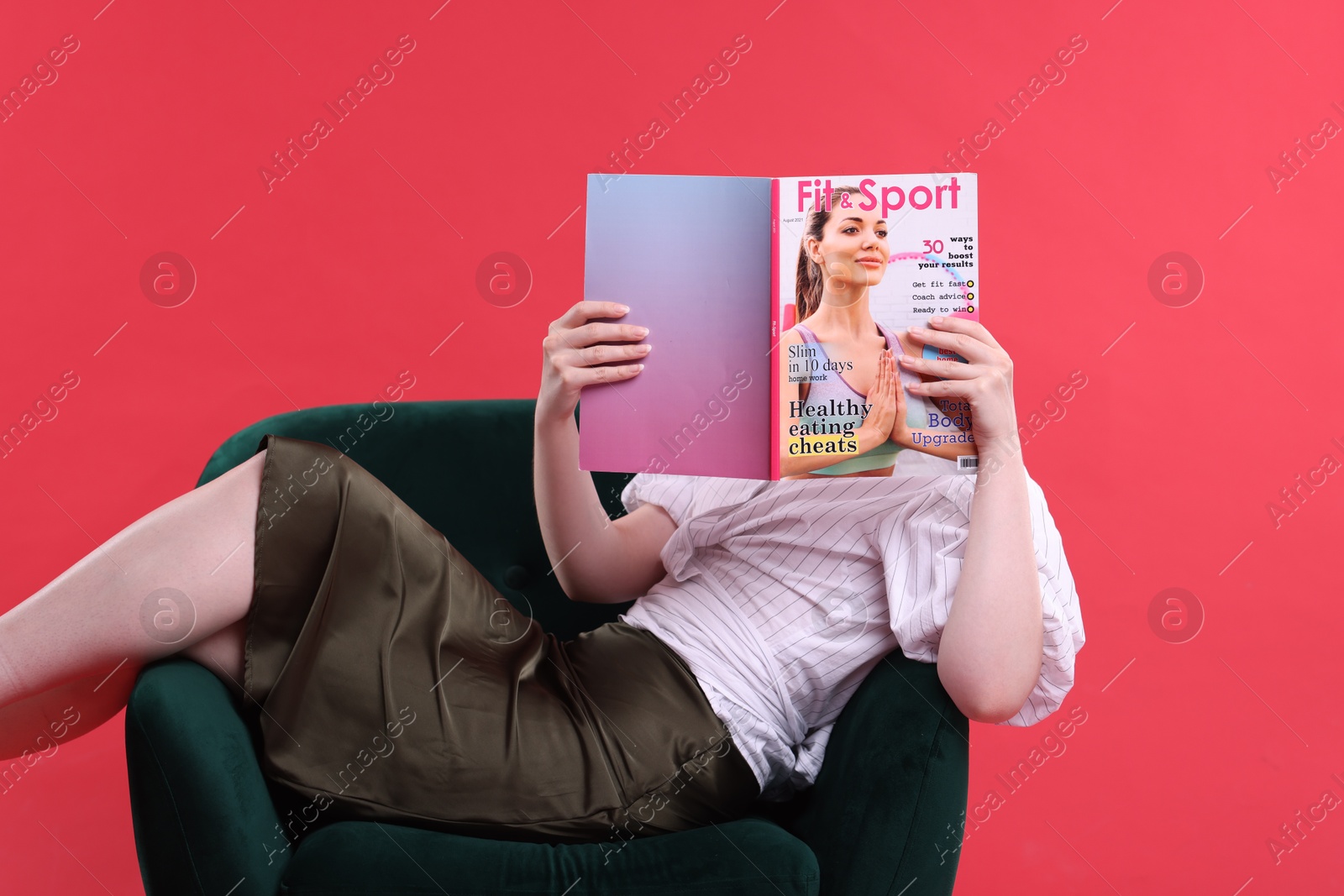 Woman with lifestyle magazine on armchair against red background Photo of Woman with lifestyle magazine on armchair against red background