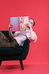 Photo of Woman with lifestyle magazine on armchair against red background
