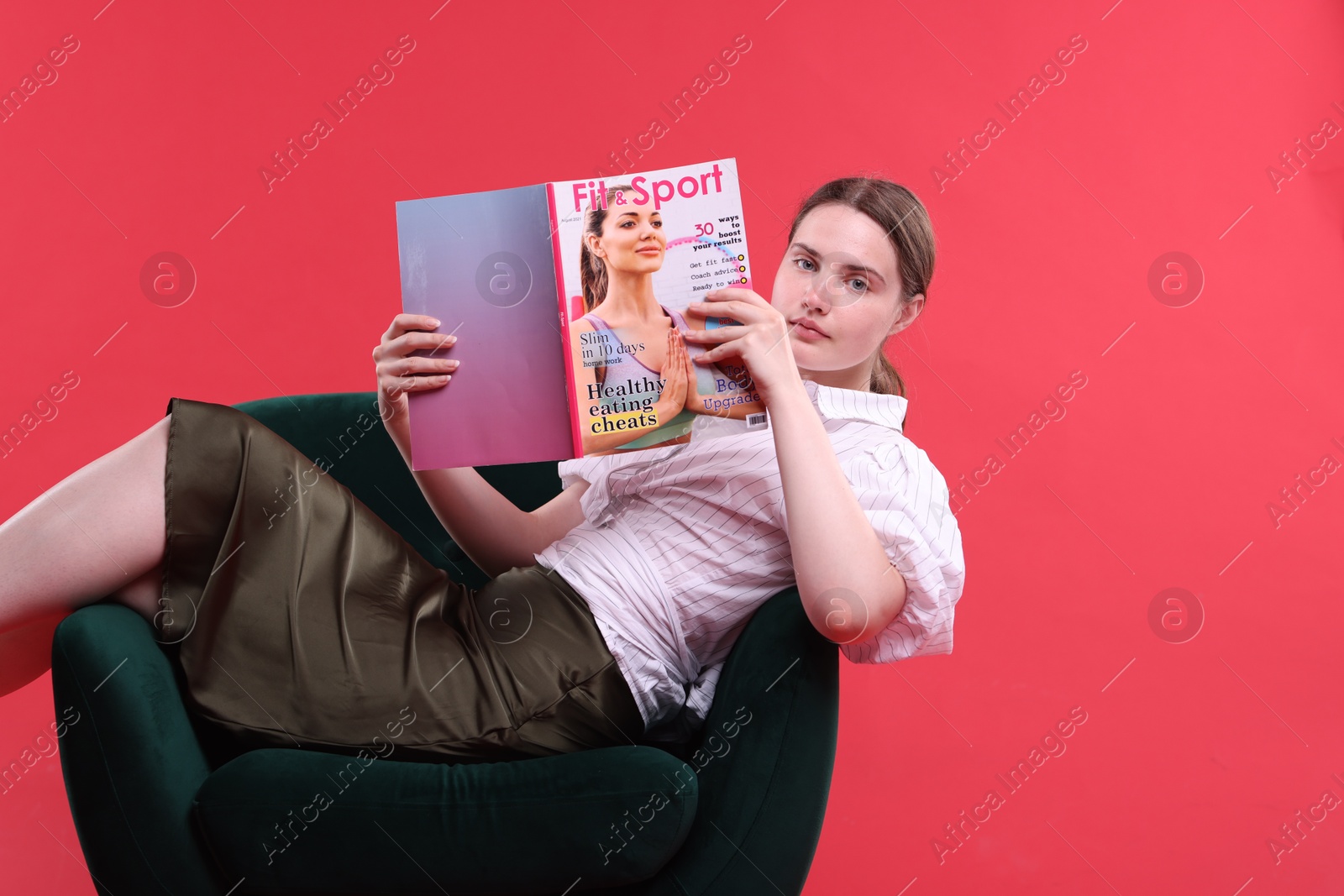 Woman with lifestyle magazine on armchair against red background, space for text Photo of Woman with lifestyle magazine on armchair against red background, space for text