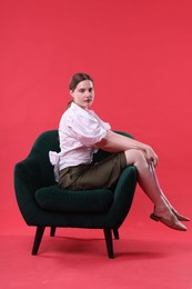 Photo of Beautiful young woman sitting on armchair against red background