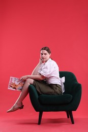 Photo of Woman with lifestyle magazine on armchair against red background