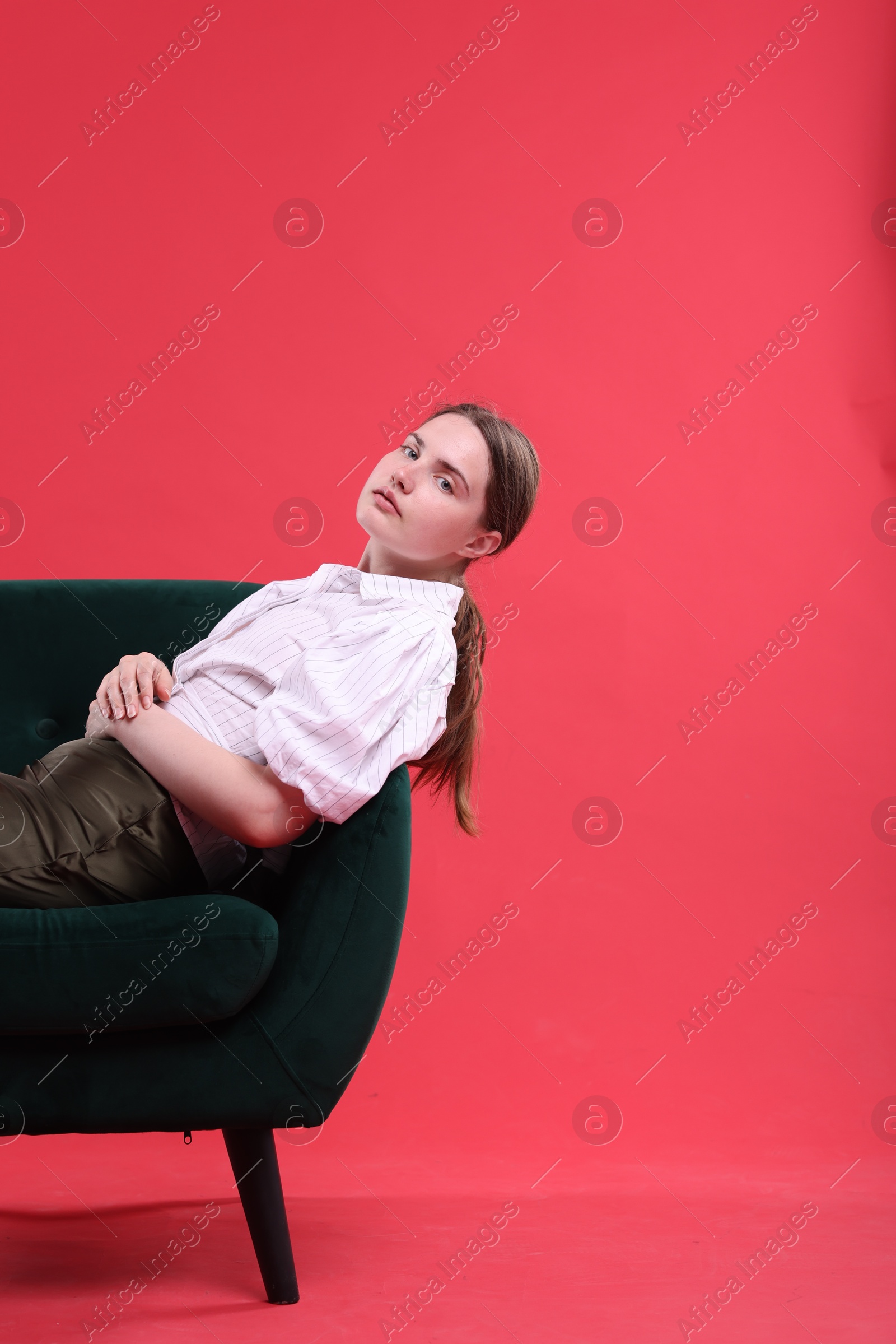 Beautiful young woman sitting on armchair against red background, space for text Photo of Beautiful young woman sitting on armchair against red background, space for text