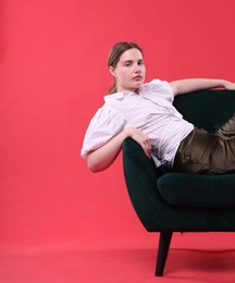 Photo of Beautiful young woman sitting on armchair against red background, space for text