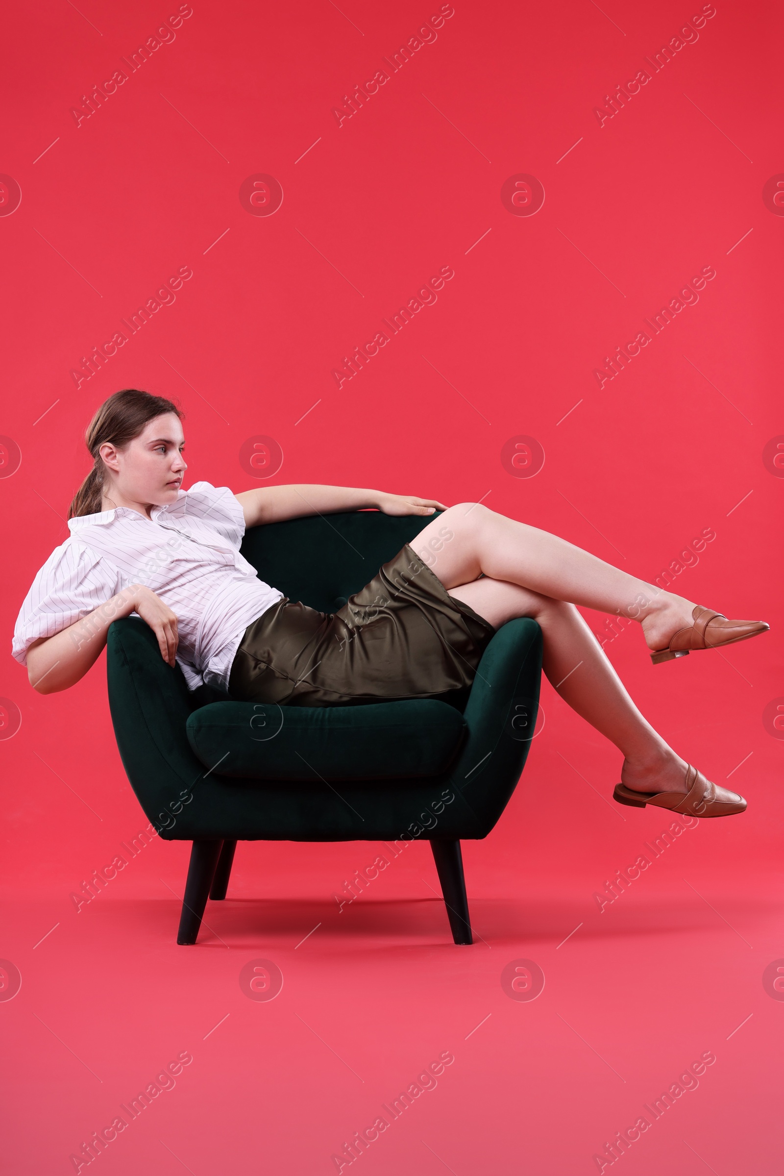 Beautiful young woman sitting on armchair against red background Photo of Beautiful young woman sitting on armchair against red background