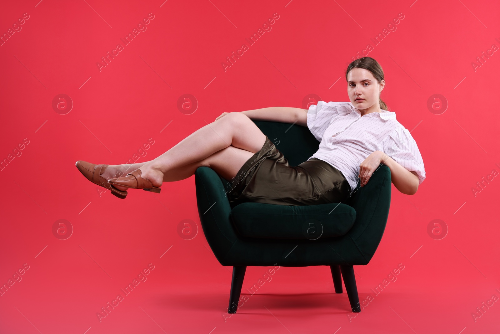 Beautiful young woman sitting on armchair against red background Photo of Beautiful young woman sitting on armchair against red background
