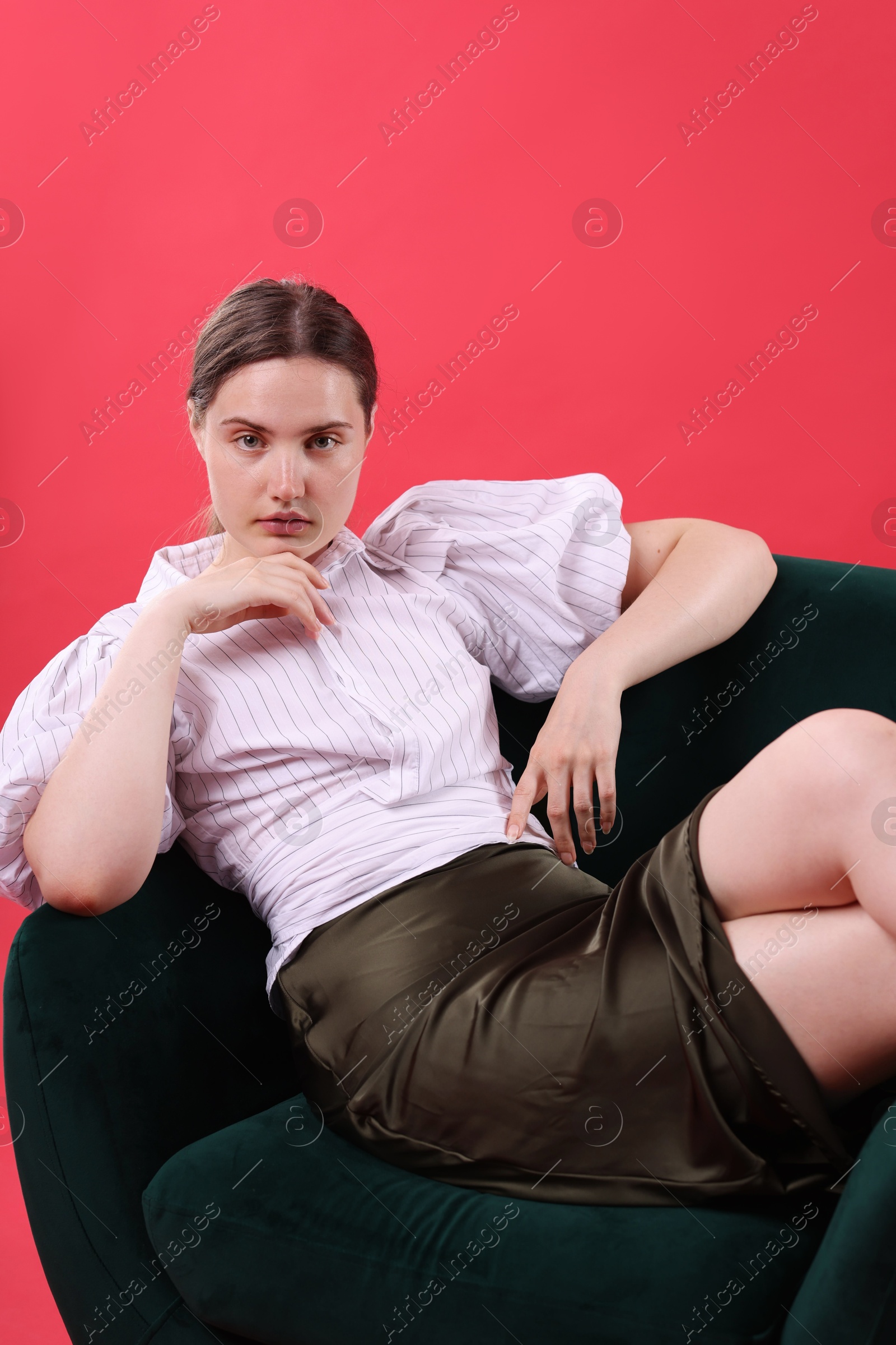Beautiful young woman sitting on armchair against red background Photo of Beautiful young woman sitting on armchair against red background