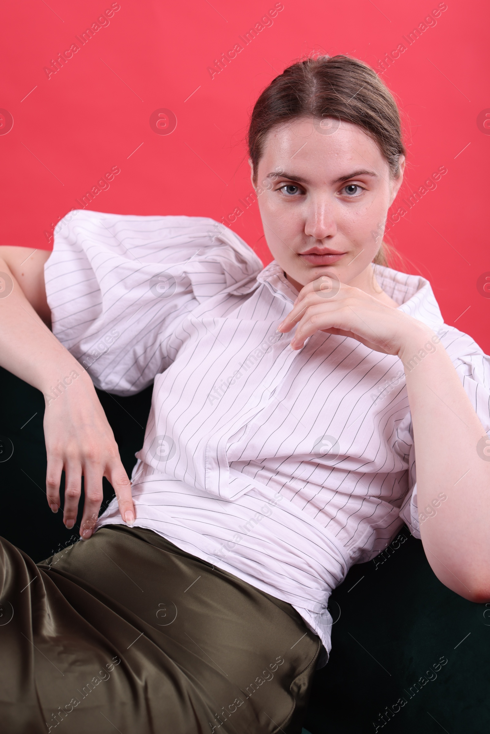 Beautiful young woman sitting on armchair against red background Photo of Beautiful young woman sitting on armchair against red background
