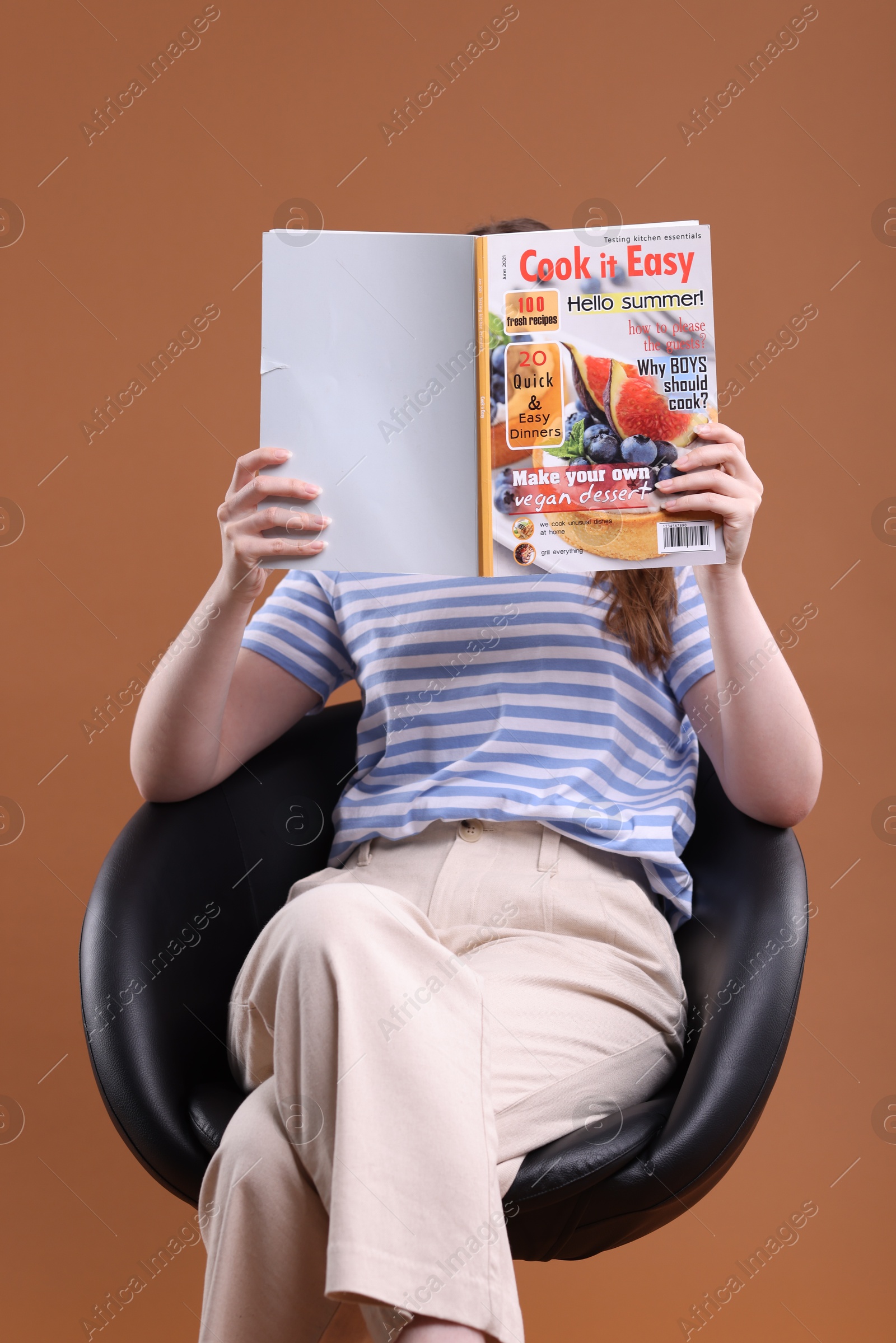 Woman with lifestyle magazine on armchair against brown background Photo of Woman with lifestyle magazine on armchair against brown background