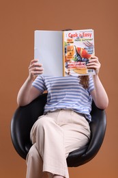 Photo of Woman with lifestyle magazine on armchair against brown background