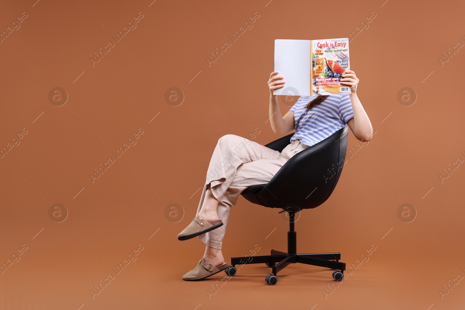 Woman with lifestyle magazine on armchair against brown background, space for text Photo of Woman with lifestyle magazine on armchair against brown background, space for text