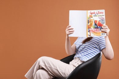 Photo of Woman with lifestyle magazine on armchair against brown background, space for text