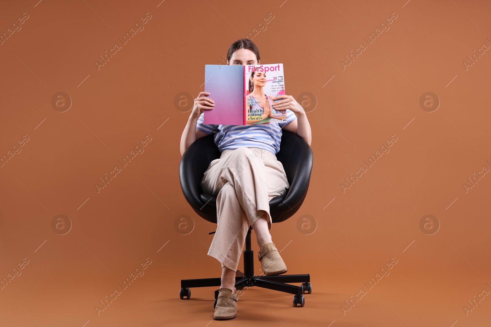 Woman with lifestyle magazine on armchair against brown background Photo of Woman with lifestyle magazine on armchair against brown background