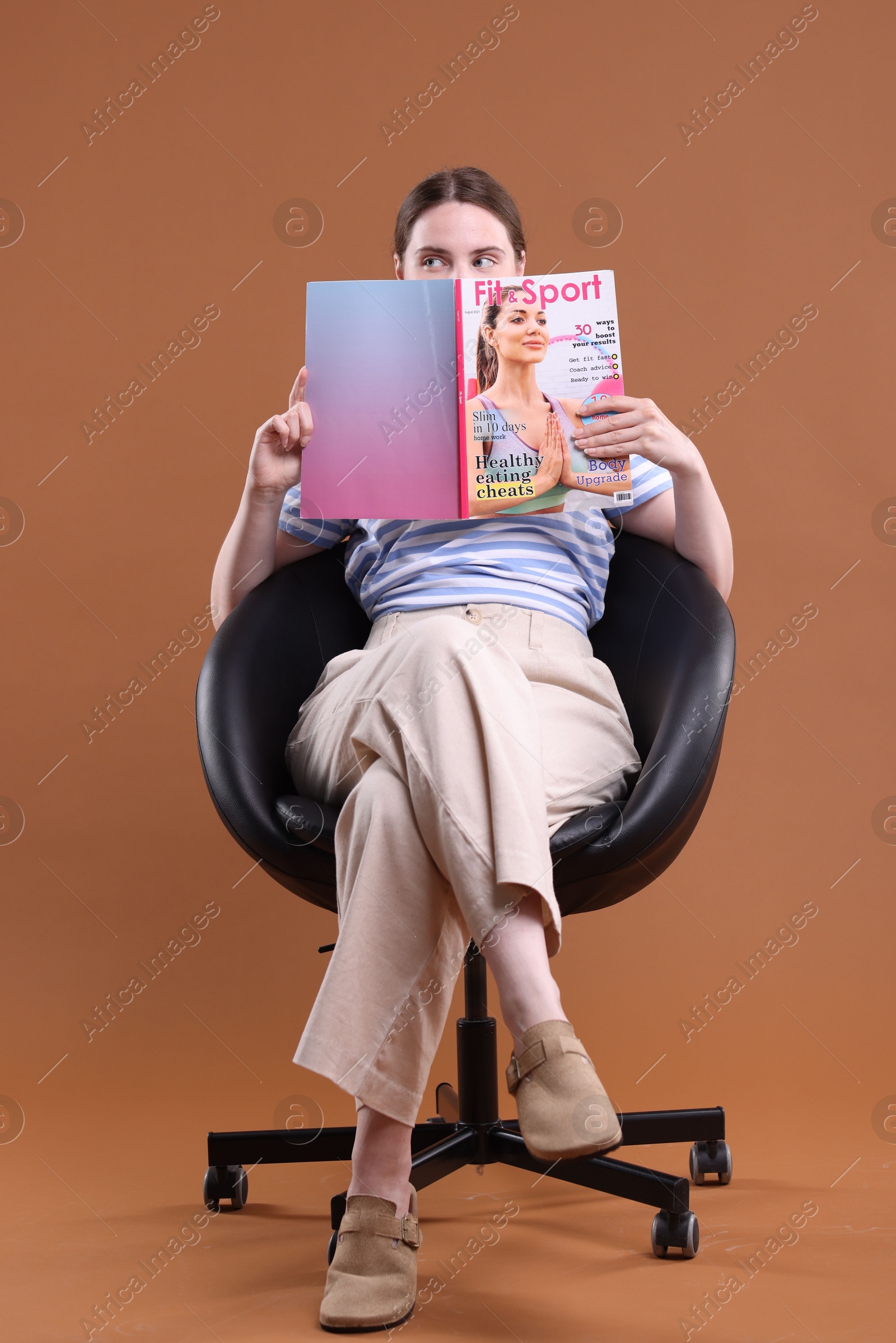 Woman with lifestyle magazine on armchair against brown background Photo of Woman with lifestyle magazine on armchair against brown background