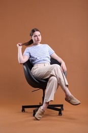 Photo of Beautiful young woman sitting on armchair against brown background