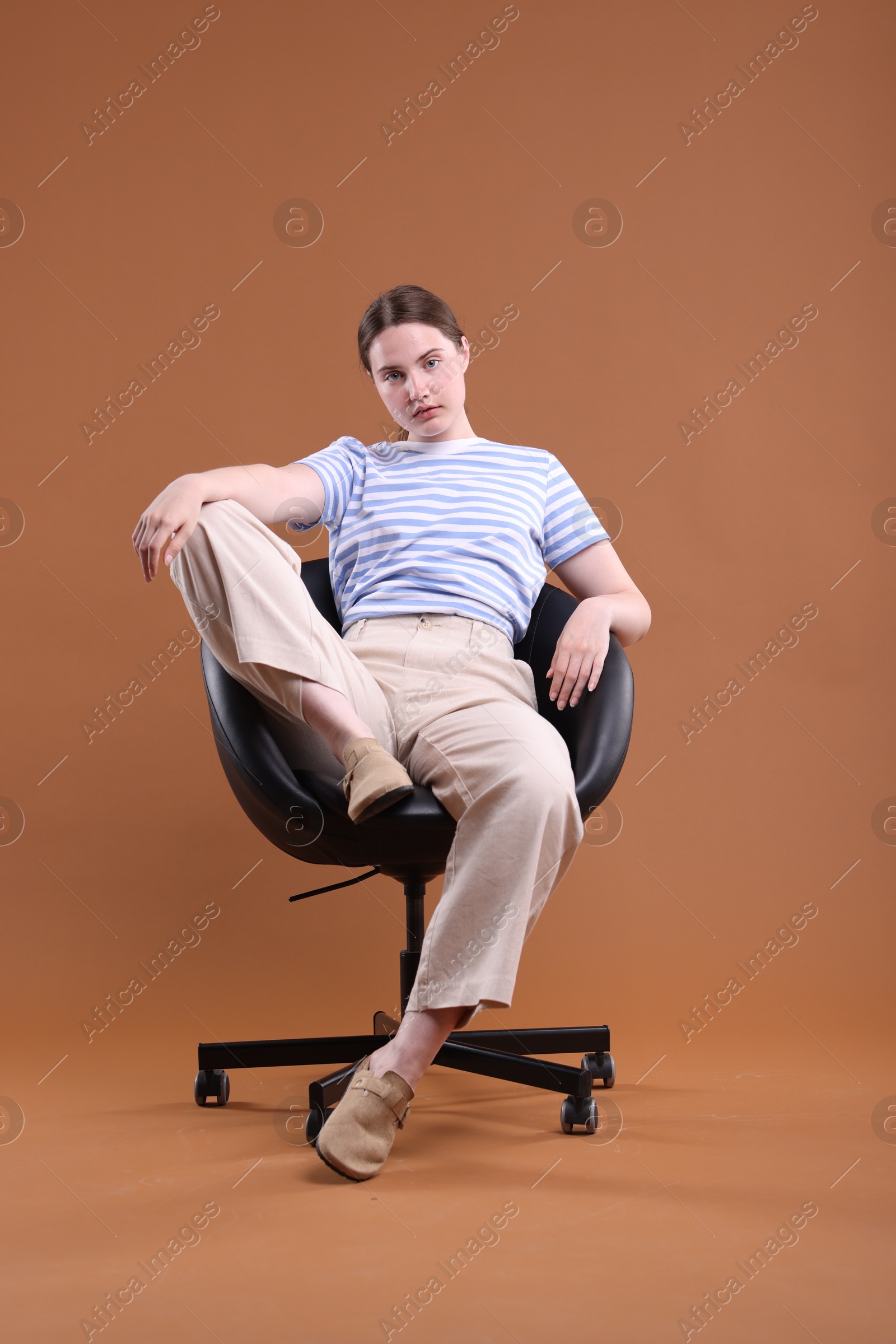 Beautiful young woman sitting on armchair against brown background Photo of Beautiful young woman sitting on armchair against brown background